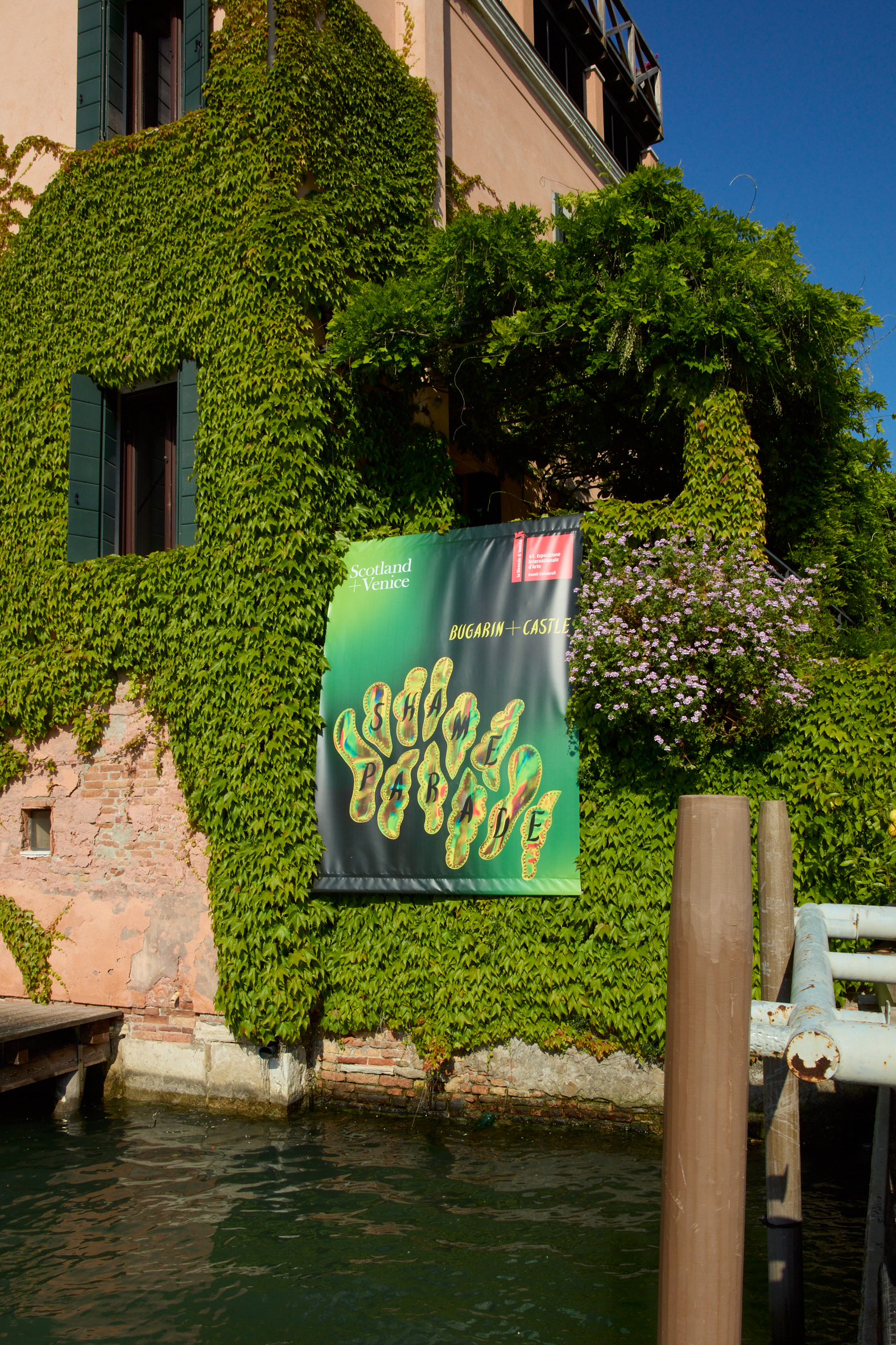 Side of building in Venice covered in greenery with large Shame Parade banner